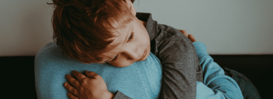 Garçon qui pleure sur l'épaule de son parent - Le deuil durant l'enfance - Blogue | Clinique de Psychologie Québec